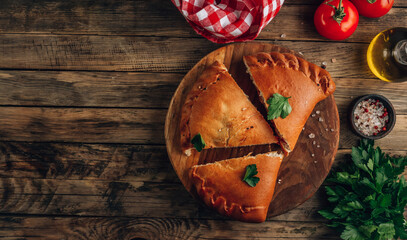 Italian food, sliced closed pizza calzone with cheese on rustic wooden background.