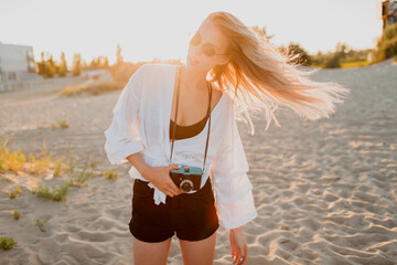 Stylish shapely girl with retro camera posing on sunny evening beach. Summer vacation. Tropical...