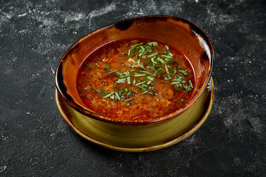 A dish of Georgian cuisine - Kharcho, beef soup with rice, walnuts and tklapi or tkemali sour sauce. Spicy soup on a dark background