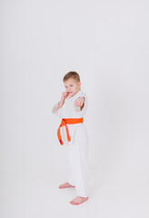 serious little boy in a white kimono with an orange belt stands at full height in a pose on a white background with space for text