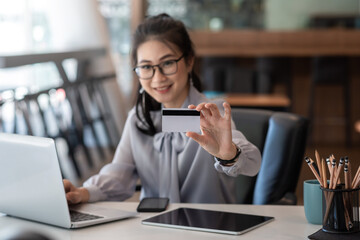 Young Asian businesswoman holding a credit card with laptop on a desk at office.