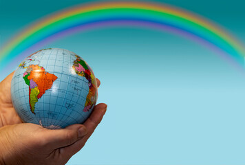 On a blue background, a globe is in the palms. A multicolored rainbow shines above him.