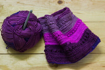 colorful ball of wool and piece of woven winter garment with crochet needle or hook against light background. copy space background for crochet knitting hobby.