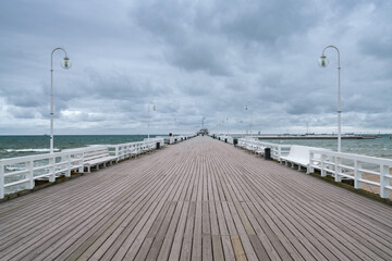 Longue jetée en bois sur la côte baltique à Sopot, Pologne avec garde-corps blanc et lampadaires par une journée froide et nuageuse. Eau verte et ciel sombre.