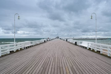 Fotobehang De Oostzee, Sopot, Polen Lange houten pier aan de Baltische kust in Sopot, Polen met witte reling en straatlantaarns op een koude, bewolkte dag. Groen water en donkere lucht.