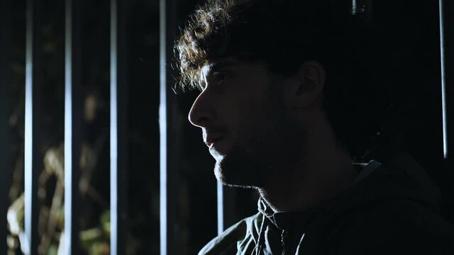 symbol of captivity - thoughtful man leaning against a gate looks away