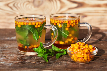 Warming green tea with sea buckthorn and mint, poured into glass mugs stands on a wooden table. The concept of a therapeutic healing drink prepared in glass