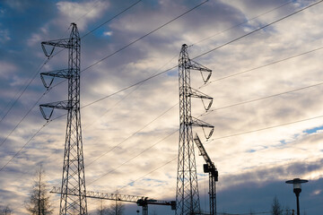 A tall construction crane against the setting sun. High voltage power pole. Machine for high-altitude lifting of building materials.
