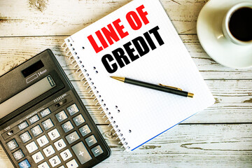 LINE OF CREDIT written on white paper near coffee and calculator on a light wooden table. Business concept