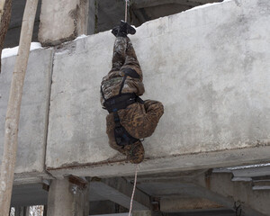 A man, a military (assault) climber descends head down (feet up) on a rope without insurance on the wall of a building. An employee of a special unit in camouflage at the training ground.