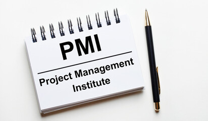 On a light background, a white notebook with the words PMI Project Management Institute and a pen.