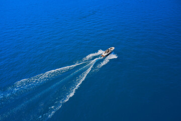 Obraz premium Drone view of a boat sailing at high speed. Aerial view of a boat in motion on blue water. luxury motor boat. Top view of a white boat sailing in the blue sea.
