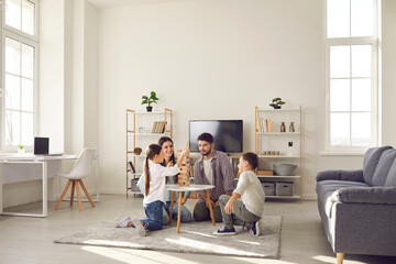 Fototapeta na wymiar Happy family father mother and two children sitting on floor and playing at home together during weekend. Family spending happy time at home and having fun with children concept
