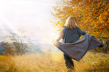 A woman of 40 years in autumn nature landscape. The blonde woman wears clothes made of wool and boots. She has a blanket.