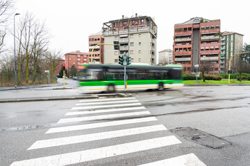 Fast moving bus in motion blur at a crossroad. Pedestrian crossing in the foreground. Milan, Italy.