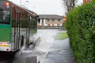 Bus flooding the sidewalk by passing over a puddle in a road. Urban environment, Milan, Italy