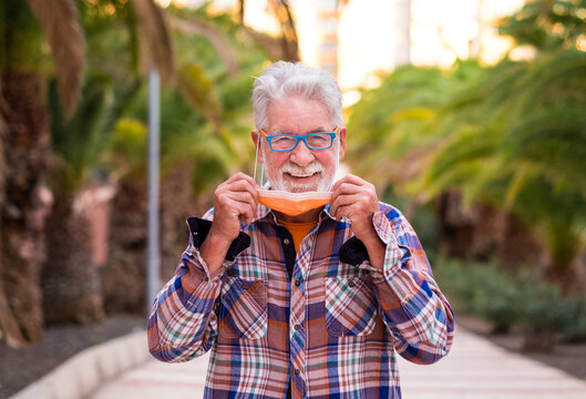 Coronavirus. A senior man takes off his surgical mask and smiles looking at camera. A relaxed pensioner in checkered shirt - Powered by Adobe