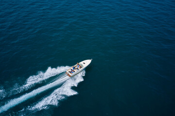 Drone view of a boat sailing across the blue clear waters. Top view of a white boat sailing to the blue sea. Motor boat in the sea. Travel - image.