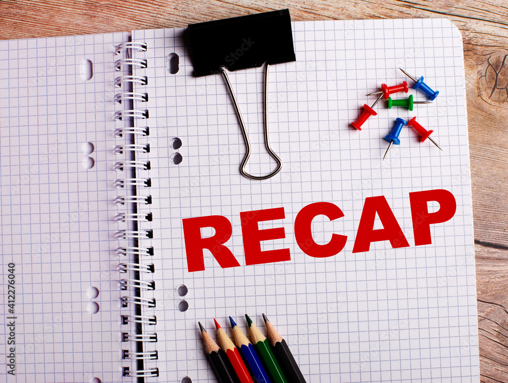 Aufkleber the word recap is written in a notebook near multi-colored pencils and buttons on a wooden backgroun