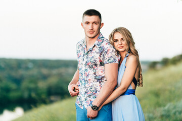 blonde girl with loose hair in a light blue dress and a guy in the light of sunset