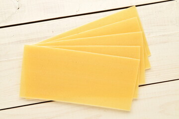 Several light yellow uncooked sheets for lasagna, close-up, on a wooden table, top view.