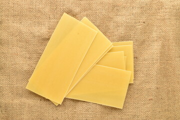 Several light yellow uncooked lasagna sheets, close-up, on sackcloth, top view.