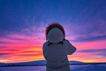 Fototapeta premium Hiker girl in down jacket photographing amazing colorful winter sunset. Travel concept.