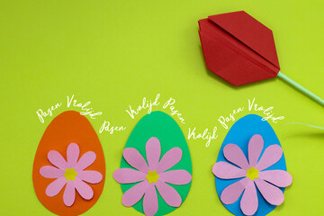 Dutch text Vrolijk Pasen (happy Easter) on a green background with colorful paper eggs, paper flowers and a red paper tulip.