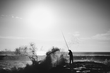 Fisherman on a pier with angry sea black and white