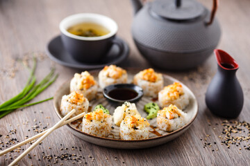 Baked sushi maki rolls with prawns and crab on a plate with chopsticks, soy sauce, wasabi and ginger. Japanese traditional fish food closeup served for lunch in modern gourmet restaurant
