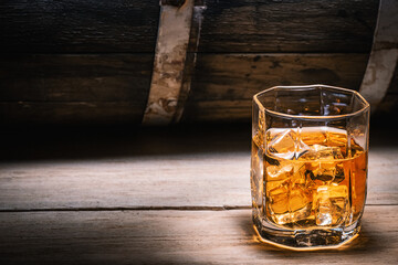 Glass of whiskey or brandy with ice close-up on the background of a wooden barrel of an alcoholic drink. Whiskey brandy scotch cognac strong alcoholic drinks.