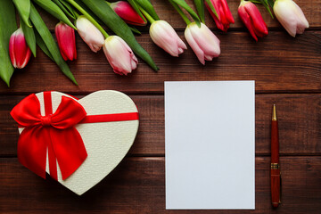 Naklejka na ściany i meble Beautiful bouquet of tulips on a dark wooden background with heart-shaped gift box, empty blank of paper and pen. Festive template for greetings. Copy space for text. Selective focus, close-up