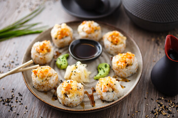 Baked sushi maki rolls with prawns and crab on a plate with chopsticks, soy sauce, wasabi and ginger. Japanese traditional fish food closeup served for lunch in modern gourmet restaurant