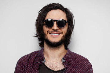 Studio portrait of young smiling guy with round sunglasses on white background.