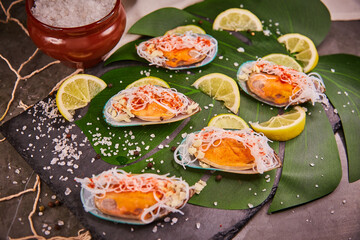 Mussels with vermicelli, lying on a leaf of a green plant in a restaurant. Funchosa vermicelli (glass noodles) with seafood and lemon, salt and spices scattered on the table