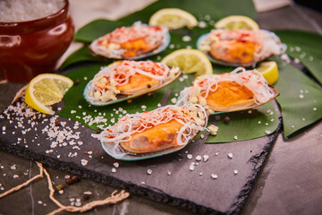 Mussels with vermicelli, lying on a leaf of a green plant in a restaurant. Funchosa vermicelli (glass noodles) with seafood and lemon, salt and spices scattered on the table