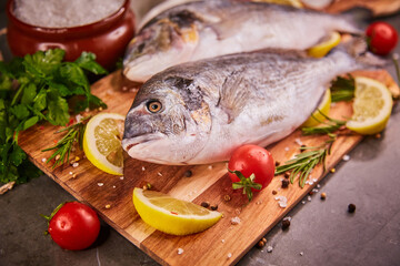 Fresh raw dorado fish. Sea bream, lying on a wooden board on a gray table with herbs and salt and spices. Dorado and ingredients for cooking on the table. Close-up