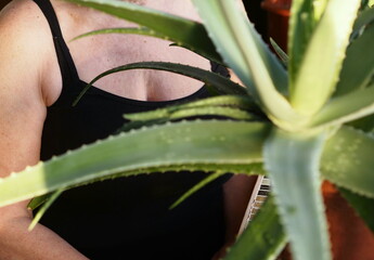 Aloe Vera medicinal plant against the background of an elderly woman in a black T shirt, symbolizing the timely recognition and treatment of breast cancer in older women.