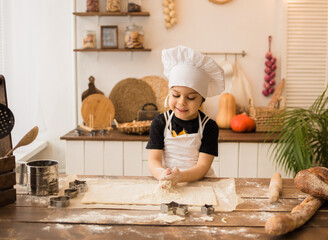 little cook in a white apron and cap kneads a place at the table in the kitchen