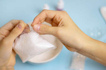 a child makes a bath bomb from sea salt, citric acid, soda, dye and flavor on a blue background,...