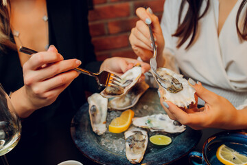 Flat lay of caucasian hands holding oysters with other seafood dishes on a dark table.
