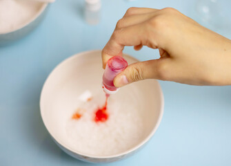 a child makes a bath bomb from sea salt, citric acid, soda, dye and flavor on a blue background,...