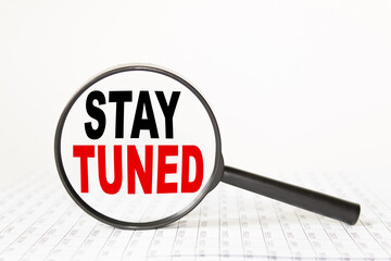 words STAY TUNED in a magnifying glass on a white background. business concept