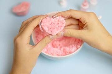 a child makes a bath bomb from sea salt, citric acid, soda, dye and flavor on a blue background,...