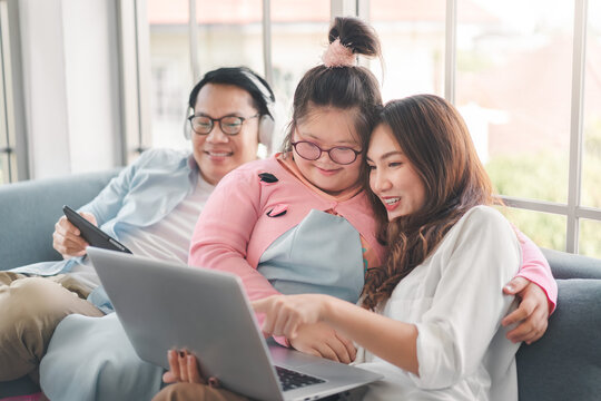 Happy Asian Family With Their Daughter Down Syndrome Child Sitting On Sofa  Have Fun Using Laptop Watch A Movie For Education , Enjoy Relax Timing Together, Activity Happy Family Lifestyle Concept.