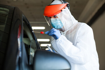 Medical worker in personal protective equipment swabbing a person in a car drive through mobile testing center