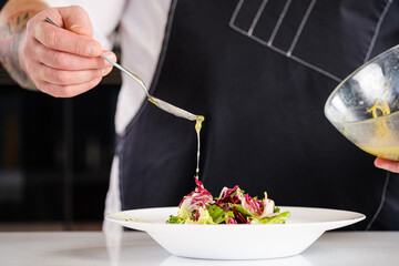 Chef finishing her plate. The cook pours the salad from a spoon with sauce.