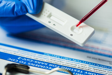 Medical laboratory technician placing blood sample specimen on quick rapid diagnostic test using...