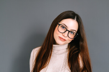 Portrait of smiling young caucasian woman in eyeglasses on gray background looking at camera.