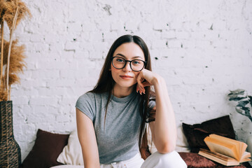 Authentic lifestyle portrait of attractive young caucasian woman in eyeglasses sitting on a sofa at home and looking at camera.